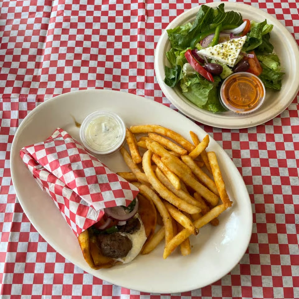 Alpha Gyro Grill's gyro with fries and a side Greek salad on a red and white checkered tablecloth.