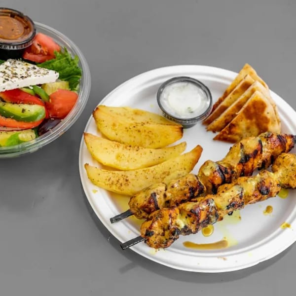 Greek chicken souvlaki skewers, potato wedges, pita bread, and a side salad with feta.