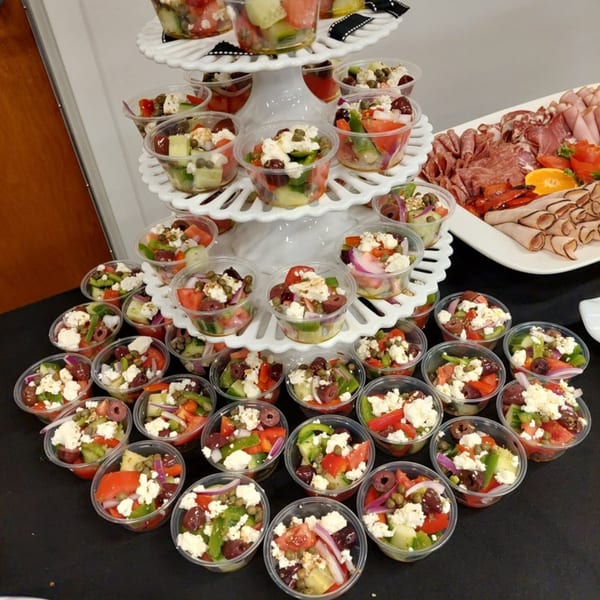 Individual Greek salads with feta, olives, and vegetables, alongside a platter of deli meats.