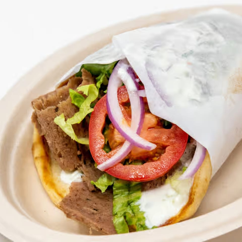 A delicious Alpha Gyro Grill gyro, wrapped in paper, filled with meat, lettuce, tomatoes, onions, and tzatziki.