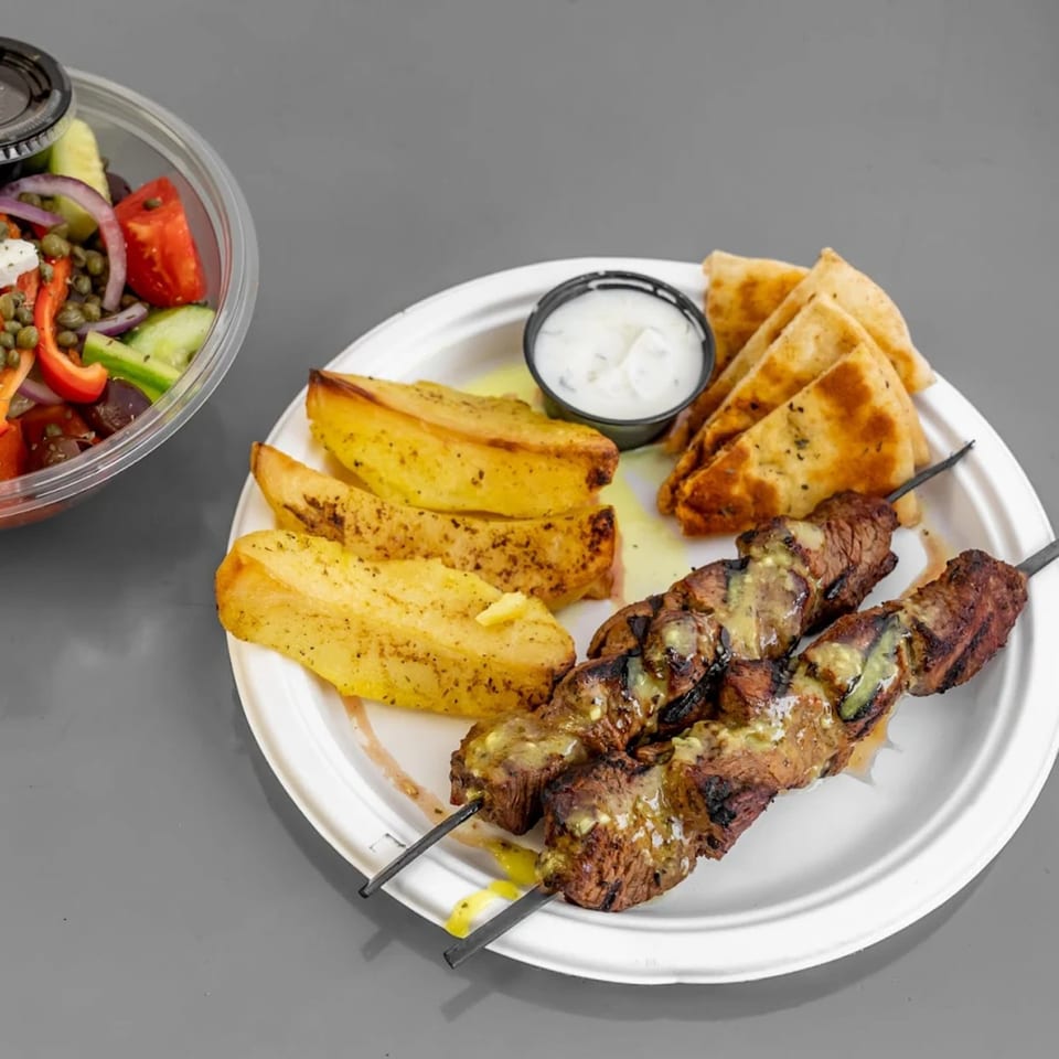 Two Alpha Gyro Grill souvlaki skewers, Greek potatoes, pita bread, tzatziki, and a side salad.