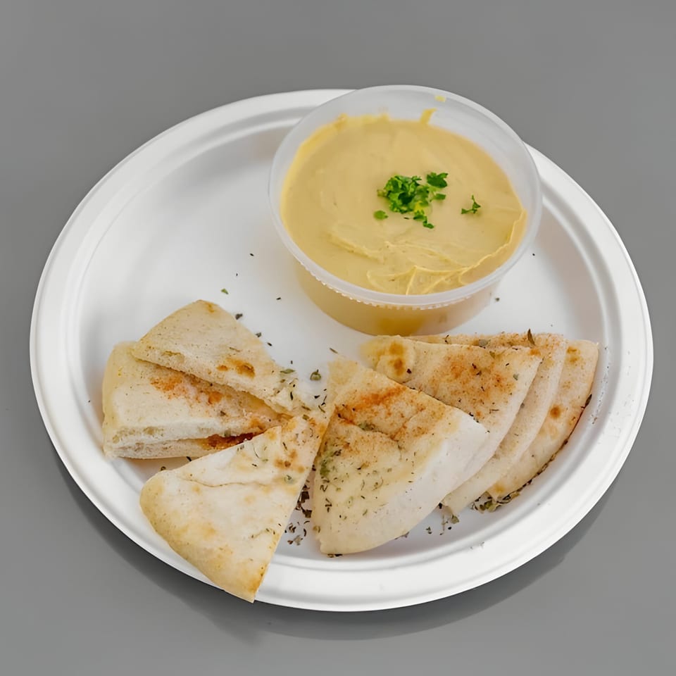 Hummus in a plastic container with pita bread triangles seasoned with herbs on a white plate.