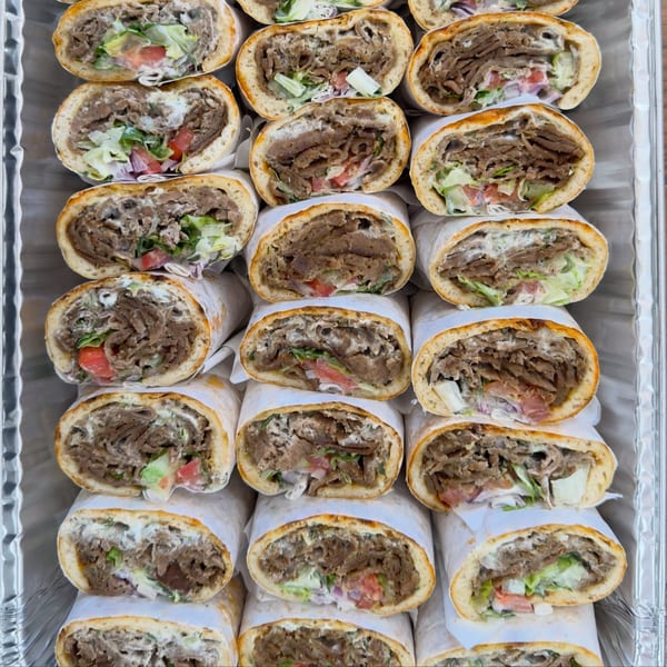 Rows of Alpha Gyro Grill gyros, filled with meat, lettuce, tomato, and sauce, in a foil tray.